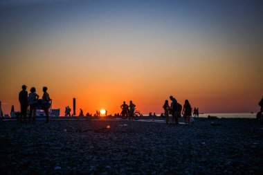 Siyah siluetler sahilde günbatımı turuncu Güneşin ışığında insan. Çakıl plaj Batum batımında sahilde turistler günbatımı karşılamak..