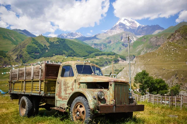 Old truck in a mountainous area against the mountain top of Kazbek in Georgia. Retro car in green mountain valley in bright sun.