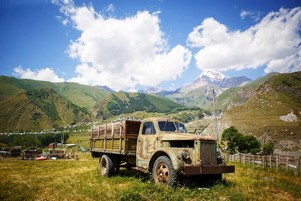 Old truck in a mountainous area against the mountain top of Kazbek in Georgia. Retro car in green mountain valley in bright sun.