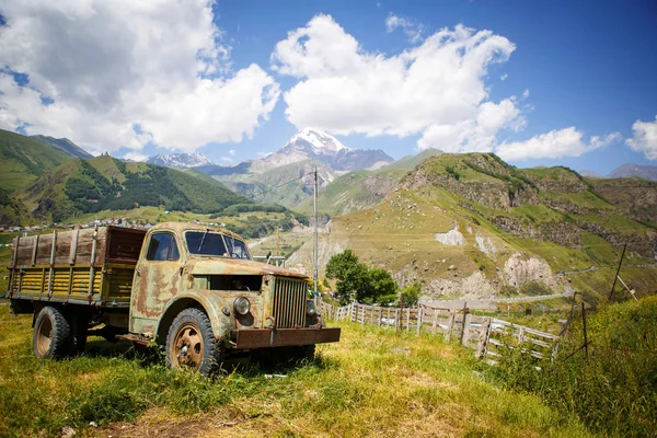 Old truck in a mountainous area against the mountain top of Kazbek in Georgia. Retro car in green mountain valley in bright sun.