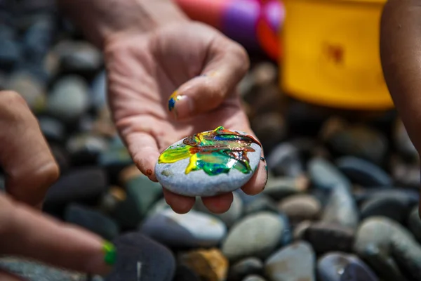 Children's entertainment on a pebble beach-paint stones. Painted with finger paints stones and jars of paint, leisure for the child, children's creativity.