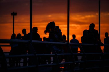 Siyah siluetler günbatımı turuncu ışık sahildeki insan. Lamba mesaj ve akşam güneş koyu turuncu ışık bir yürüyüş için çit arkasındaki kişi profilleri. Gürcistan, Batum dolgu