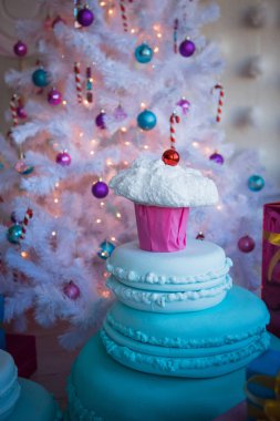 Kek ve büyük çikolata şeklinde Noel süsleri. Nazik bir stil ve altın ışıkları çelenk beyaz yapay Noel ağacı Noel oyuncaklar. Çizgili şeker kamışı, pembe ve mavi topları yakın çekim.