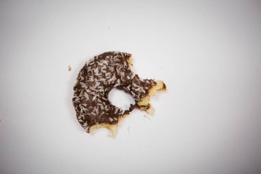 Isırılmış bir çörek beyaz bir arka planda yatıyor. Hindistan cevizi ile yarım yenmiş çikolata donut bir parçası.