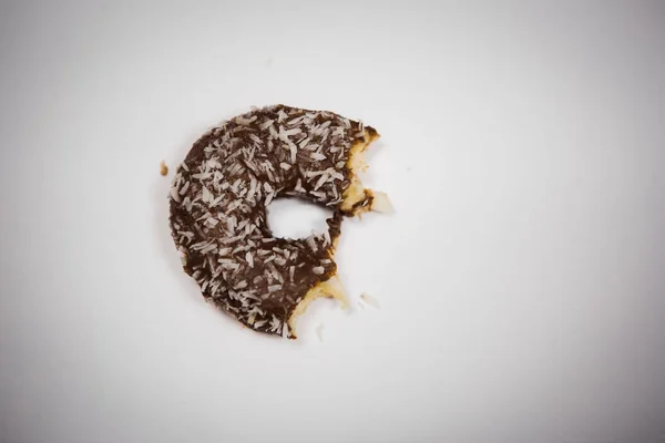 A bitten donut lies on a white background. A piece of half-eaten chocolate doughnut with coconut.
