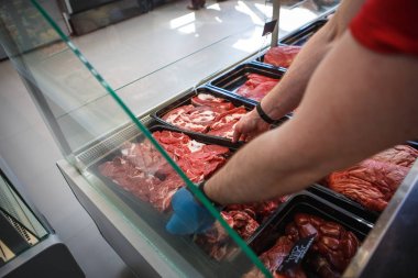 Kasap dükkanının vitrininde tepsilerde çiğ et. Satıcı eti siyah tepsilerde sergiliyor