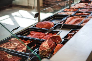 Kasap dükkanının vitrininde tepsilerde çiğ et. Satıcı eti siyah tepsilerde sergiliyor