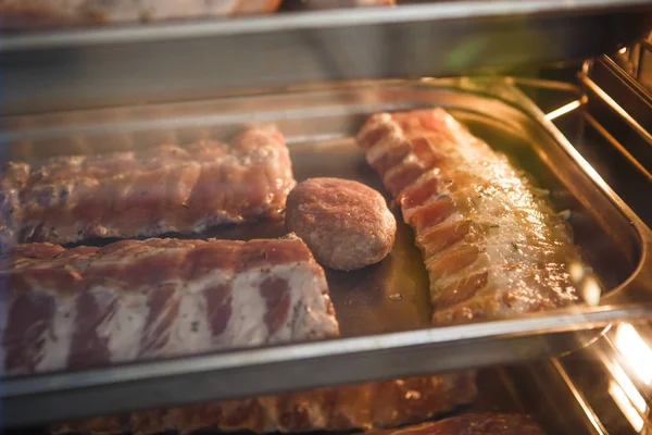 Smoked meat products in the oven smokehouse. A man holding a tray of smoked meat products