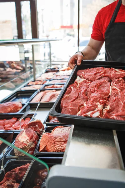 Raw meat in trays in the window of a butcher shop. The seller puts the meat on display in black trays