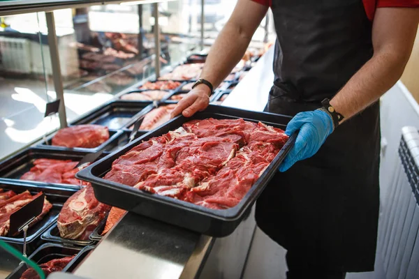 Raw meat in trays in the window of a butcher shop. The seller puts the meat on display in black trays