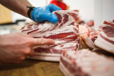 Et kesme ve doğrama işlemi. Elinde balta ve testere olan eldivenli bir adam eti özel bir tahta masada keser, kancalara asılı çiğ et parçaları.