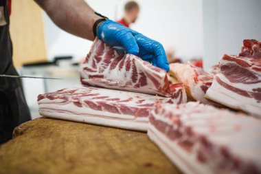 Et kesme ve doğrama işlemi. Elinde balta ve testere olan eldivenli bir adam eti özel bir tahta masada keser, kancalara asılı çiğ et parçaları.