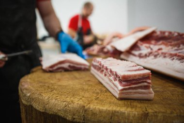 Et kesme ve doğrama işlemi. Elinde balta ve testere olan eldivenli bir adam eti özel bir tahta masada keser, kancalara asılı çiğ et parçaları.