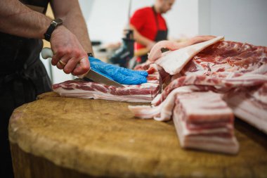 Et kesme ve doğrama işlemi. Elinde balta ve testere olan eldivenli bir adam eti özel bir tahta masada keser, kancalara asılı çiğ et parçaları.