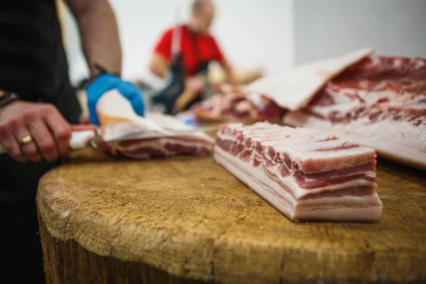 Et kesme ve doğrama işlemi. Elinde balta ve testere olan eldivenli bir adam eti özel bir tahta masada keser, kancalara asılı çiğ et parçaları.