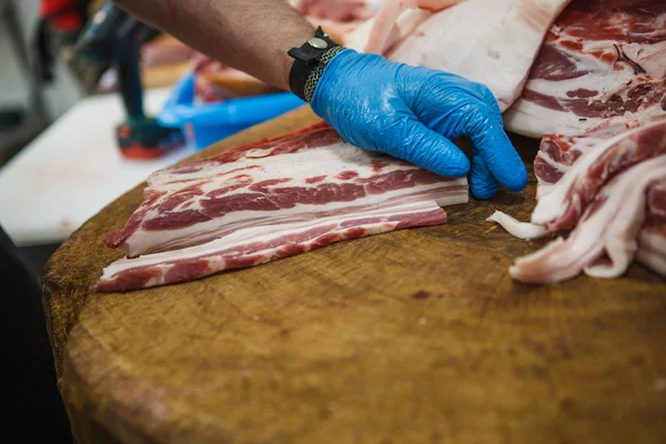 The process of cutting and chopping meat. A man in gloves with an axe and a saw cuts the meat on a special wooden table, pieces of raw meat hanging on hooks