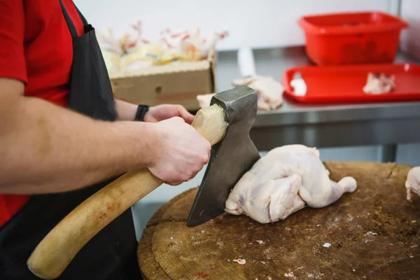 切肉的过程 一个戴着手套 戴着斧头和锯的男人把肉切在一张特殊的木桌上 一块生肉挂在钩子上 — 图库照片