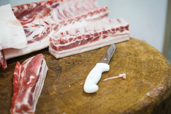 The process of cutting and chopping meat. A man in gloves with an axe and a saw cuts the meat on a special wooden table, pieces of raw meat hanging on hooks