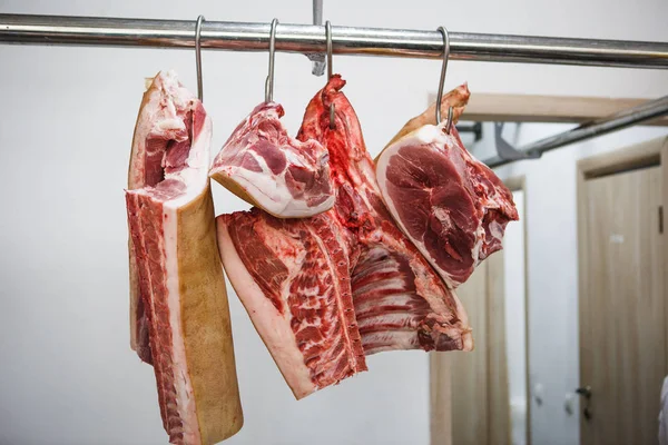 The process of cutting and chopping meat. A man in gloves with an axe and a saw cuts the meat on a special wooden table, pieces of raw meat hanging on hooks