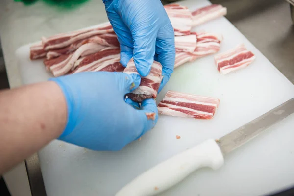 The process of preparing meat products. Gloved hands are molded from ground beef and bacon patties