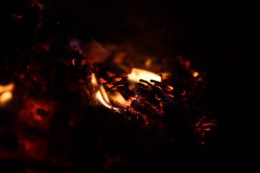 Karanlıkta yangın ateşi yakın çekim. Bir kamp ateşi Turuncu alevler, yangında közler ve konileri