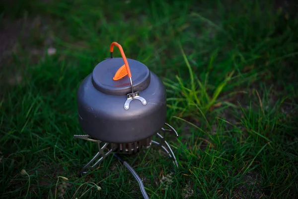 A small grey camping teapot stands on the grass. Use in the campaign of special camping utensils.