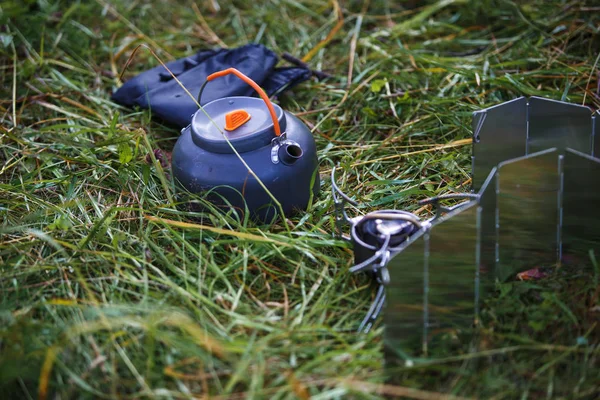 A small grey camping teapot stands on the grass. Use in the campaign of special camping utensils.