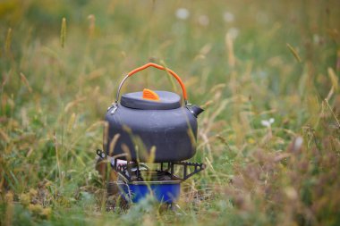 Küçük bir gri kamp çaydanlığı çimüzerinde duruyor. Özel kamp gereçleri kampanyasında kullanın.