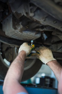 Servis istasyonunda araba tamiri. Direksiyonsuz asansörde arabayı tamir eden, lastiği tutan ve mekanik işleri tutan tulumda bir tamircinin elleri.