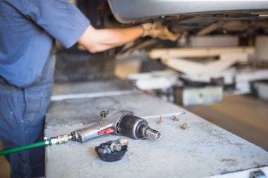Servis istasyonunda araba tamiri. Direksiyonsuz asansörde arabayı tamir eden, lastiği tutan ve mekanik işleri tutan tulumda bir tamircinin elleri.