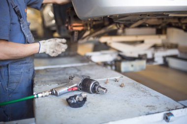 Servis istasyonunda araba tamiri. Direksiyonsuz asansörde arabayı tamir eden, lastiği tutan ve mekanik işleri tutan tulumda bir tamircinin elleri.