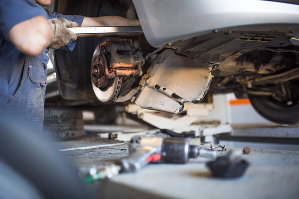 Ремонт автомобилей на автозаправке. Руки механика в комбинезоне ремонтируют автомобиль на лифте без колеса, держат шины и механические работы
.