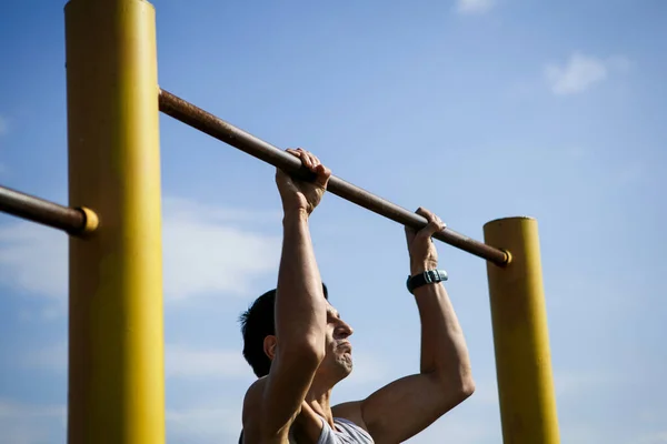 A young man of Caucasian appearance pulls himself up on a horizontal bar. The guy is hanging on one arm. Healthy lifestyle, affordable outdoor sports — Stock Image Young Man Caucasian Appearance Pulls Himself Horizontal Bar Guy Hanging Royalty Free Stock Photos