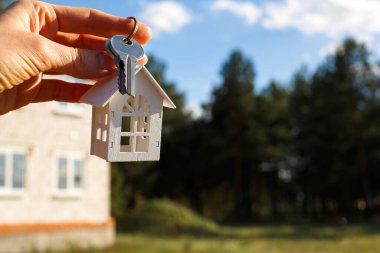 Tamamlanmamış bir evin arka planında tahta anahtarlık ve anahtarlar var. Taşınma hayali kuran kulübe, kırsal bir yerde ve projenin tamamlanması aşamasında. Metin için boşluk