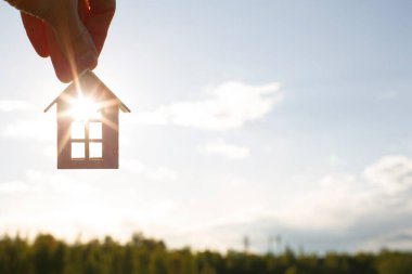 Beyaz ahşap bir ev ve anahtarlar gökyüzü ve tarlanın arka planına karşı. Evini hayal et, kırsalda bir kulübe inşa et, planla ve tasarla, projenin teslimini yap, yeni bir eve taşın..