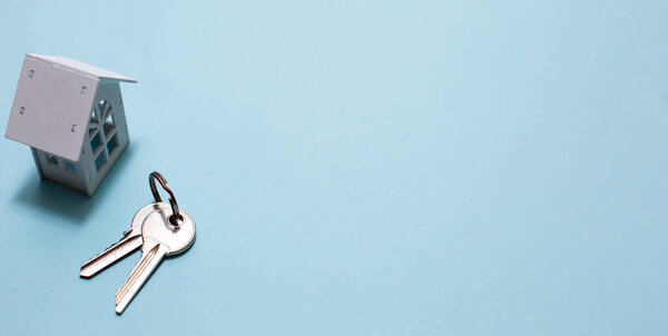 White wooden house symbol and keys on a blue background. Cottage construction concept, layout and design, architectural plan, moving to a new house, realtor, ready business. Space for text, flatly