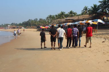 Goa, Hindistan-7 Ocak 2017. İnsanlar sahil şeridi boyunca Sinquerim 'de yürüyor. Turistler ve yerel halk, kumlu sahilde bir grup Hintli.