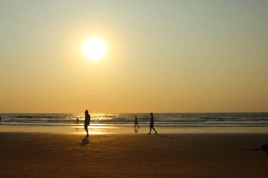 Goa, Hindistan-7 Ocak 2017. Farklı milletlerden insanlar gün batımında Hindistan 'ın kumlu sahillerinde yürürler. Siluetler turuncu gökyüzüne ve Arambol 'daki Hint okyanusuna karşı