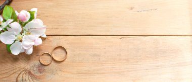 Ahşap arka planda iki altın yüzük ve beyaz elma çiçekleri. Eko-stil, kırsal bir düğün. Aşık bir çift, tören ve kayıt, detaylar, gelin ücretleri, damat sabahı. Mesaj için yer var. düzgünce.