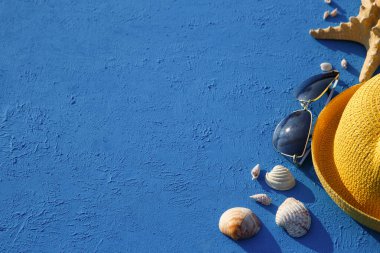 Deniz temalı plaj aksesuarları olan çerçeve: sarı hasır şapka, güneş gözlüğü, deniz yıldızı ve mavi arka planda deniz kabuğu. Tatil konsepti, deniz yolculuğu, ultraviyole koruma, yüzme. Uzayı kopyala Düz Yatay