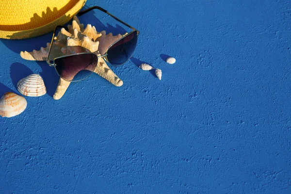 Deniz temalı plaj aksesuarları olan çerçeve: sarı hasır şapka, güneş gözlüğü, deniz yıldızı ve mavi arka planda deniz kabuğu. Tatil konsepti, deniz yolculuğu, ultraviyole koruma, yüzme. Uzayı kopyala Düz Yatay