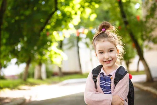 A little girl of Caucasian appearance in a school uniform with a backpack looks into the frame. Concept back to school. Elementary school, developing activities for preschoolers. Space for text