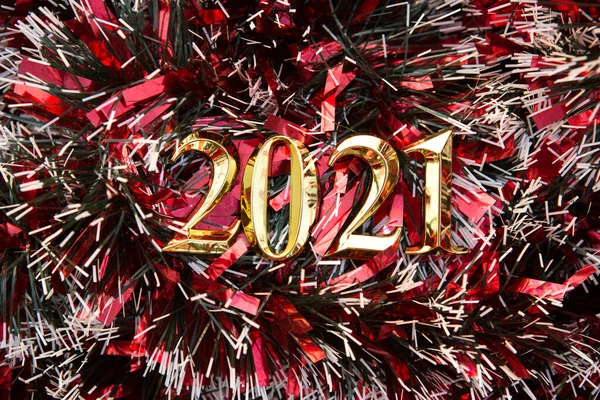 Happy new year 2021 - golden number on a red background from tinsel. Shiny Christmas decorations, a symbol of two thousand and twenty-first year. Top view, copy space.