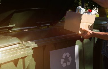 Ayrı atık toplama için konteynırların yanında elinde çöp olan bir karton kutu. Nüfusa ilişkin ekolojik farkındalık, çevreye özen, ayrılma: plastik, karton, ambalaj. 