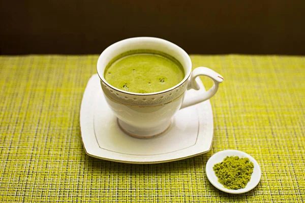 Japanese matcha green tea is poured into a white mug and on a white saucer in powder. Tea set on a textured napkin. Invigorating drink in a cafe, cooking, cheerfulness, antioxidant. space for text