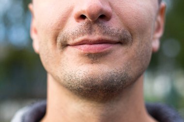 Kafkas görünümlü güzel erkek dudakları yakın plan. Yüzündeki hafif gülümseme ve kıllı sakal. Görünmez dudak kremi. Genç adam, çene, tıraş, vahşet, ustura. Metin için boşluk.