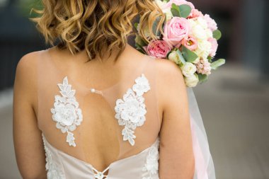 Gelinin arkasında, beyaz bir gelinlik içinde, yakın plan. Gelinin gül buketi pastel renkli, bukleli. Elbisenin süslemesinde melek kanatları var. Gelin ücretleri, düğün törenleri. Metin için boşluk