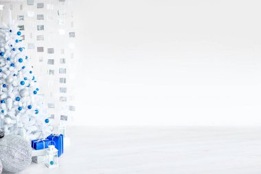 Açık gri bir odadaki Noel beyaz köknar ağacı mavi ve gümüş balonlarla süslenmiştir. Hediyelerle dolu kutular, duvardaki küplerden yapılmış dekorasyonlar. Yeni yıl. Metin için boşluk, soğuk arkaplan