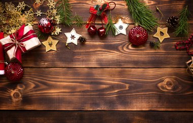 Ahşap bir arka planda Noel dekoru olan çerçeve. Yeni yıl, tatil atmosferi, yeşil ladin dalları, süslemeler: yıldızlar, hediye kutusu, boncuklar, top, çanlar, koniler. Metin için boşluk, düz uzanma