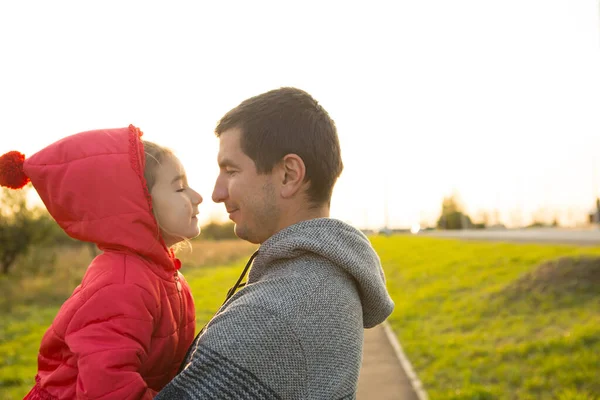 穿着红色夹克 头戴头巾的小女孩拥抱并亲吻着她的爸爸 微笑着 摸着她的鼻子 快乐的家庭 孩子的情感 父亲节 灿烂的阳光 白人的外表 案文的篇幅 — 图库照片